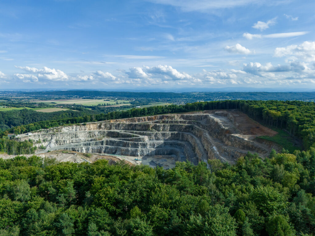 An open-pit mining operation is depicted, showcasing the extraction of minerals through a terraced, stepped approach. The surrounding environment is lush and green, indicating effective mine rehabilitation efforts. This visual representation aligns with the principles outlined in the Mining Policy Framework (MPF), which emphasizes the importance of integrating environmental stewardship into mining practices.